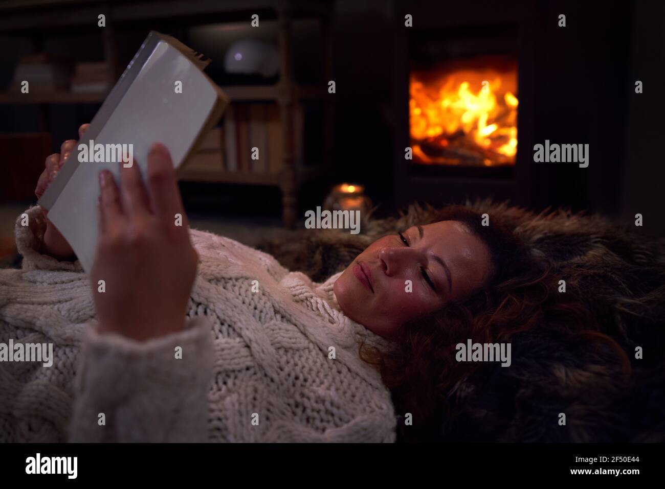 Frau entspannt Buch auf Decke am gemütlichen Kamin zu lesen Stockfoto