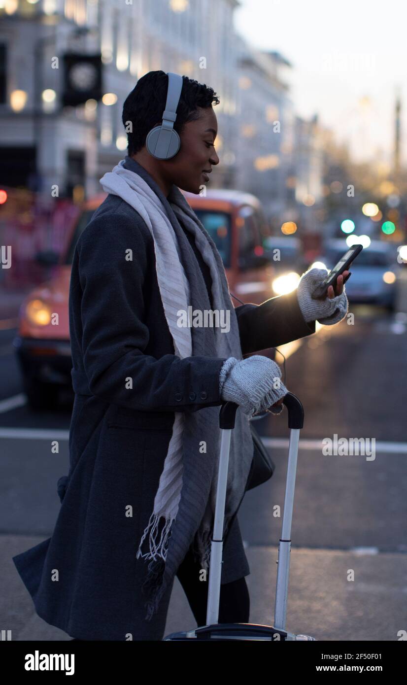 Junge Frau mit Koffer und Smartphone durch die Winterstadt Straße Stockfoto