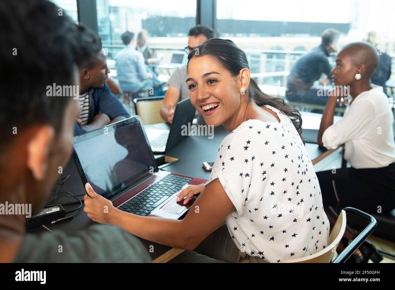 Glückliche Geschäftsfrau mit Laptop im Gespräch mit Kollegen im Büro Stockfoto