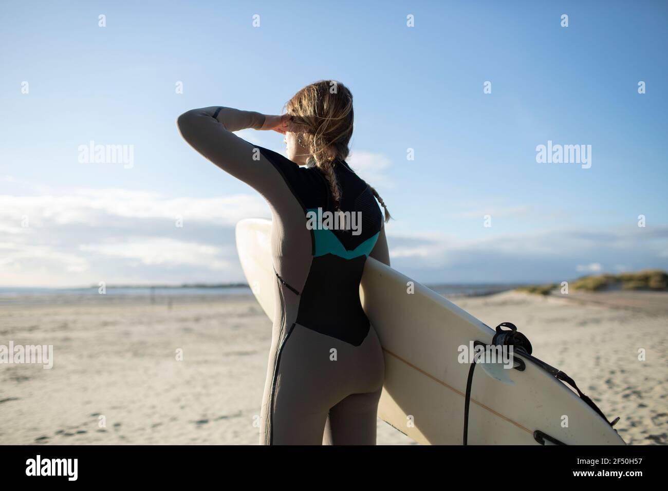 Junge Surferin mit Surfbrett, die auf den sonnigen Strand blickt Stockfoto
