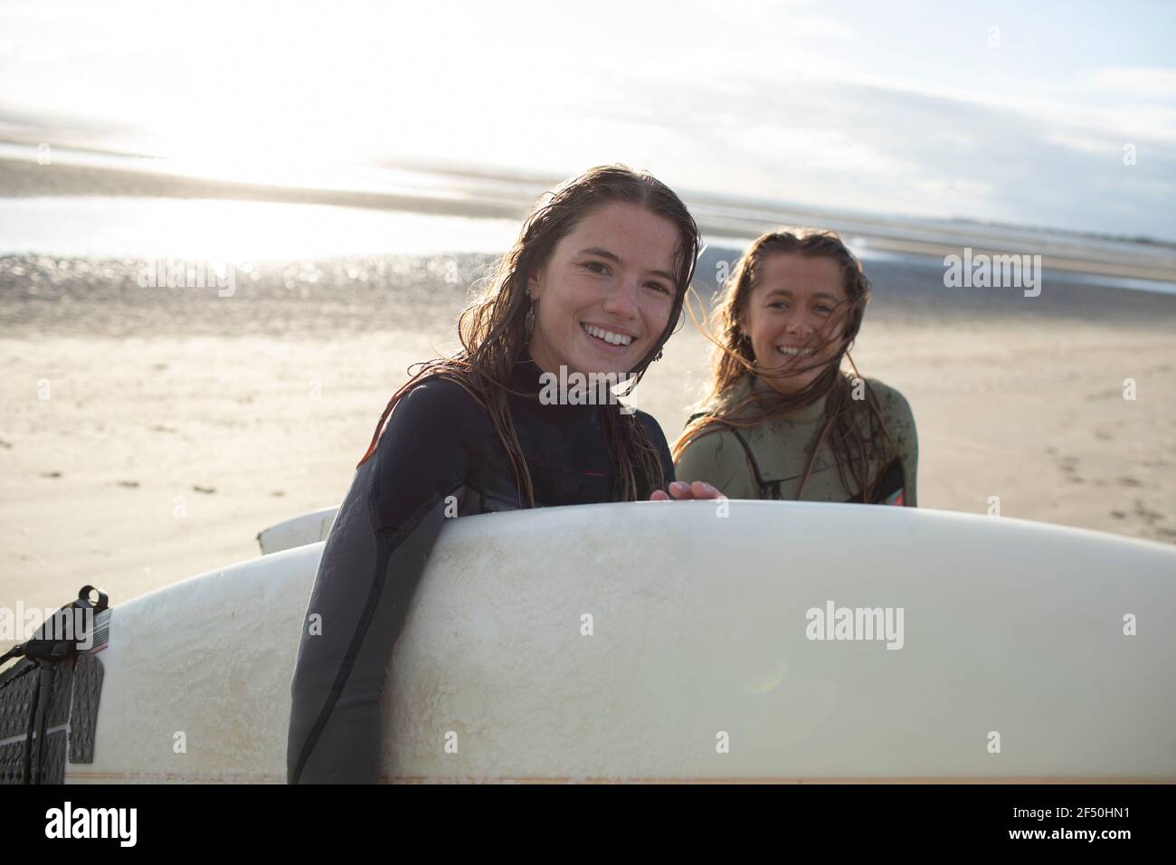 Portrait glückliche junge Surferinnen mit Surfbrett am sonnigen Strand Stockfoto