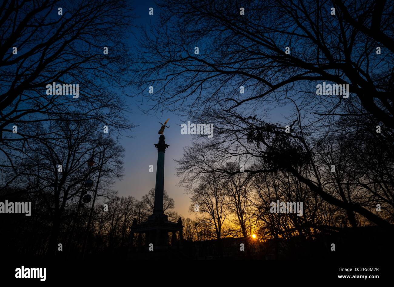 München, Deutschland. März 2021, 23rd. Die Sonne untergeht hinter der vergoldeten Figur des Friedensengels, der auf einer rund 23 Meter hohen Säule thront. Die Statue soll an den Abschluss des Friedens nach dem Krieg mit Frankreich im Jahr 1870/1871 erinnern und steht über einem kleinen Saal. Kredit: Peter Kneffel/dpa/Alamy Live Nachrichten Stockfoto