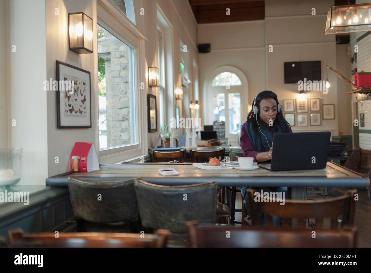 Geschäftsfrau mit Kopfhörern, die im Café am Laptop arbeitet Stockfoto