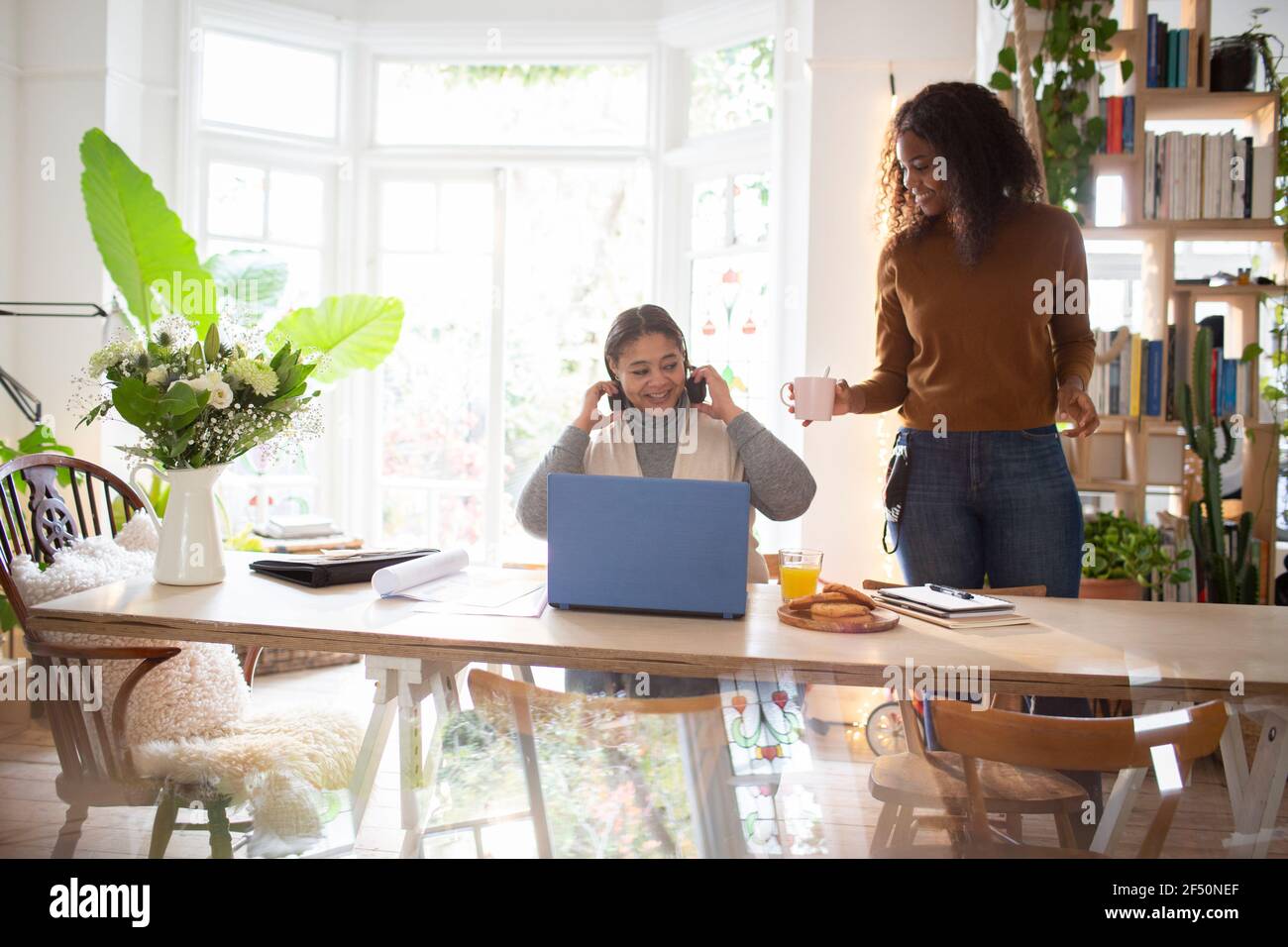 Tochter, die der Mutter Kaffee serviert, die am Laptop beim Essen arbeitet Tabelle Stockfoto