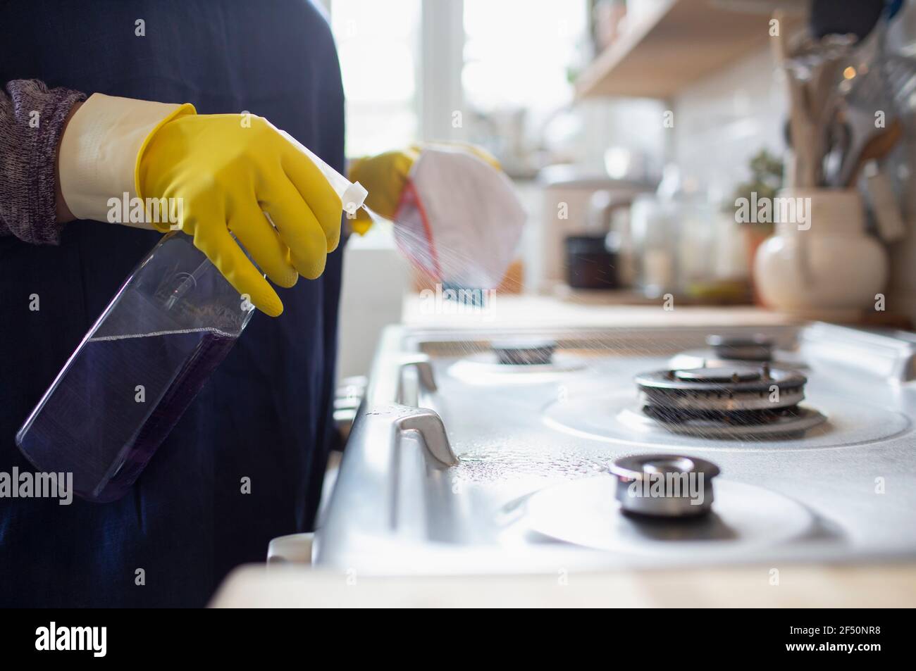 Frau in Gummihandschuhen Reinigung Küchenherd mit Sprühreiniger Stockfoto