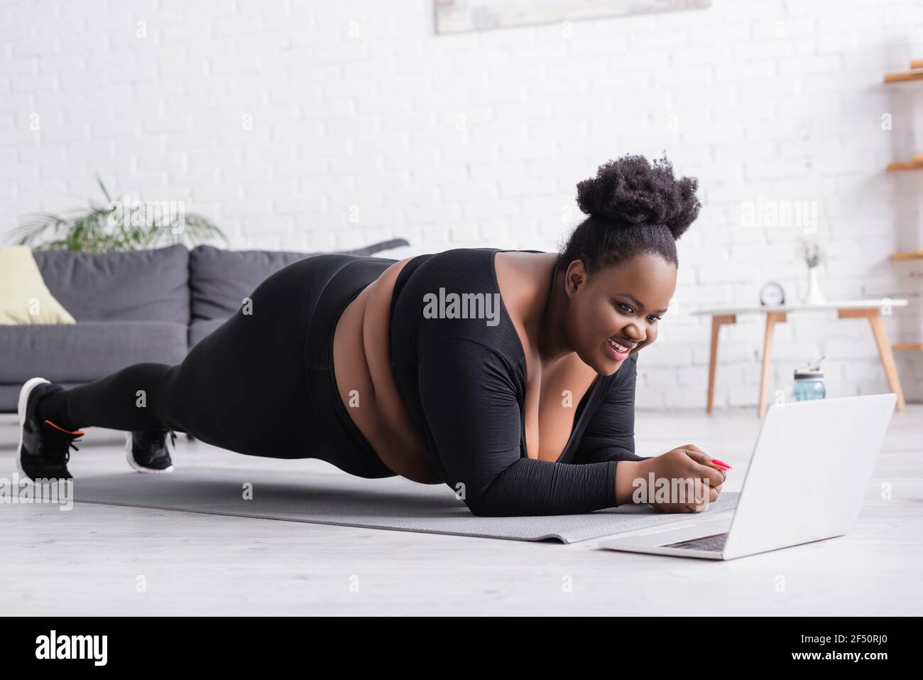 Happy african american plus size Frau beobachten Online-Sport-Training Auf  dem Laptop, während Sie Plank im Wohnzimmer tun Stockfotografie - Alamy