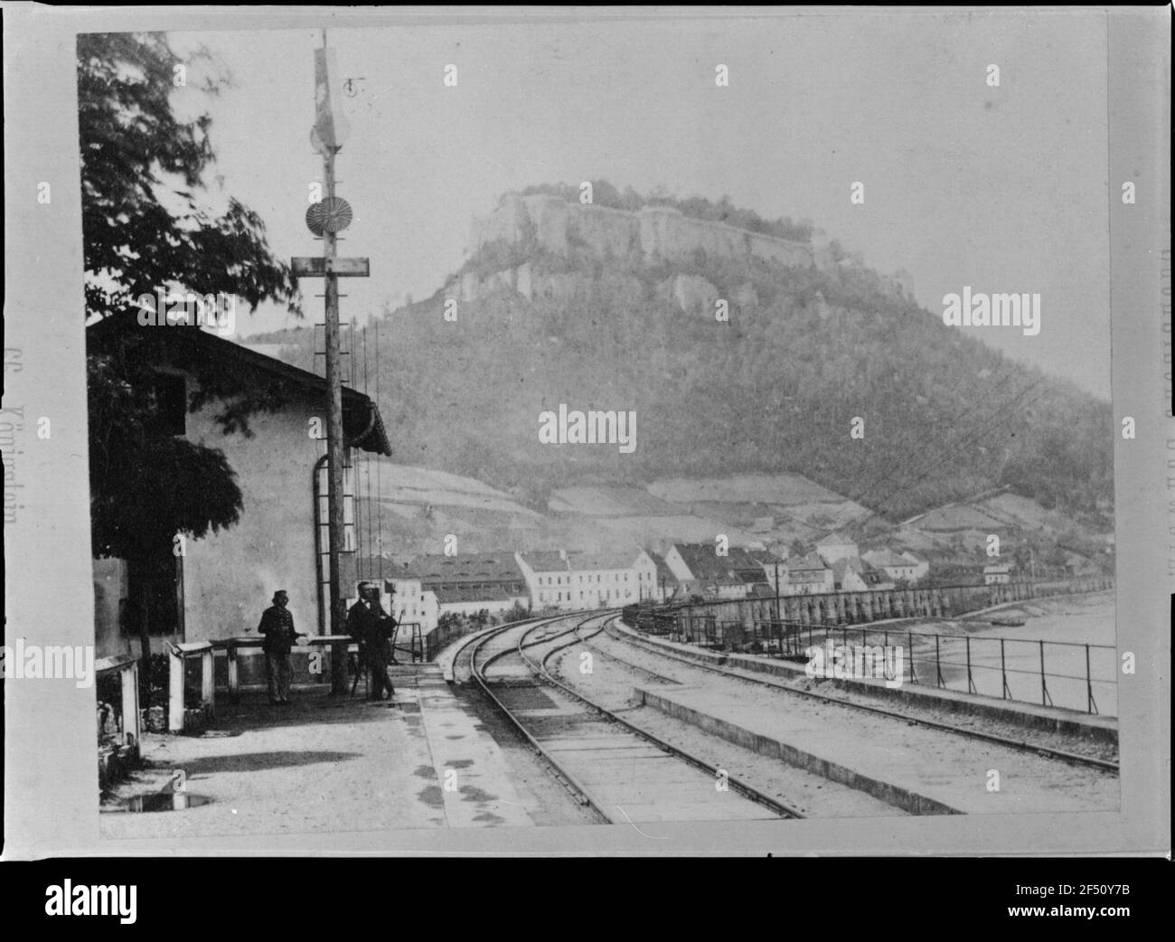 Königstein, Bahnhof. Böhmische Plattform. Blick mit drei Personen um eine Fahne / Signalmast gegen den Königstein mit Festung Stockfoto