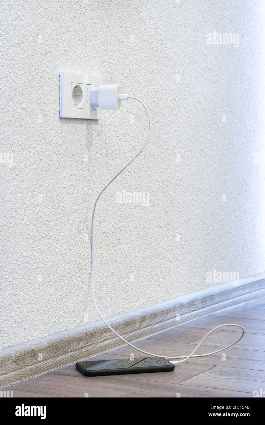 Ein Ladegerät in der Steckdose, mit dem ein Mobiltelefon aufgeladen wird Das steht auf dem Boden Stockfoto