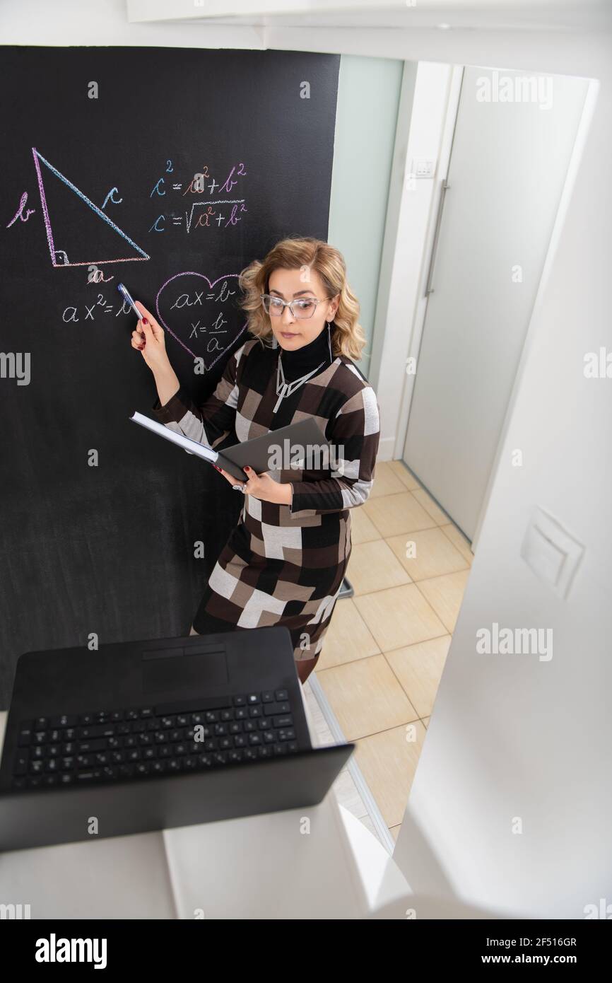 Junge Mathematiklehrerin erklärt Geometrie an der schwarzen Wand Stockfoto