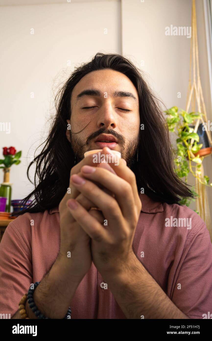 Junger langhaariger Mann meditiert mit einer Kerze in den Händen. Junger Mann betet in Spiritualität. Stockfoto