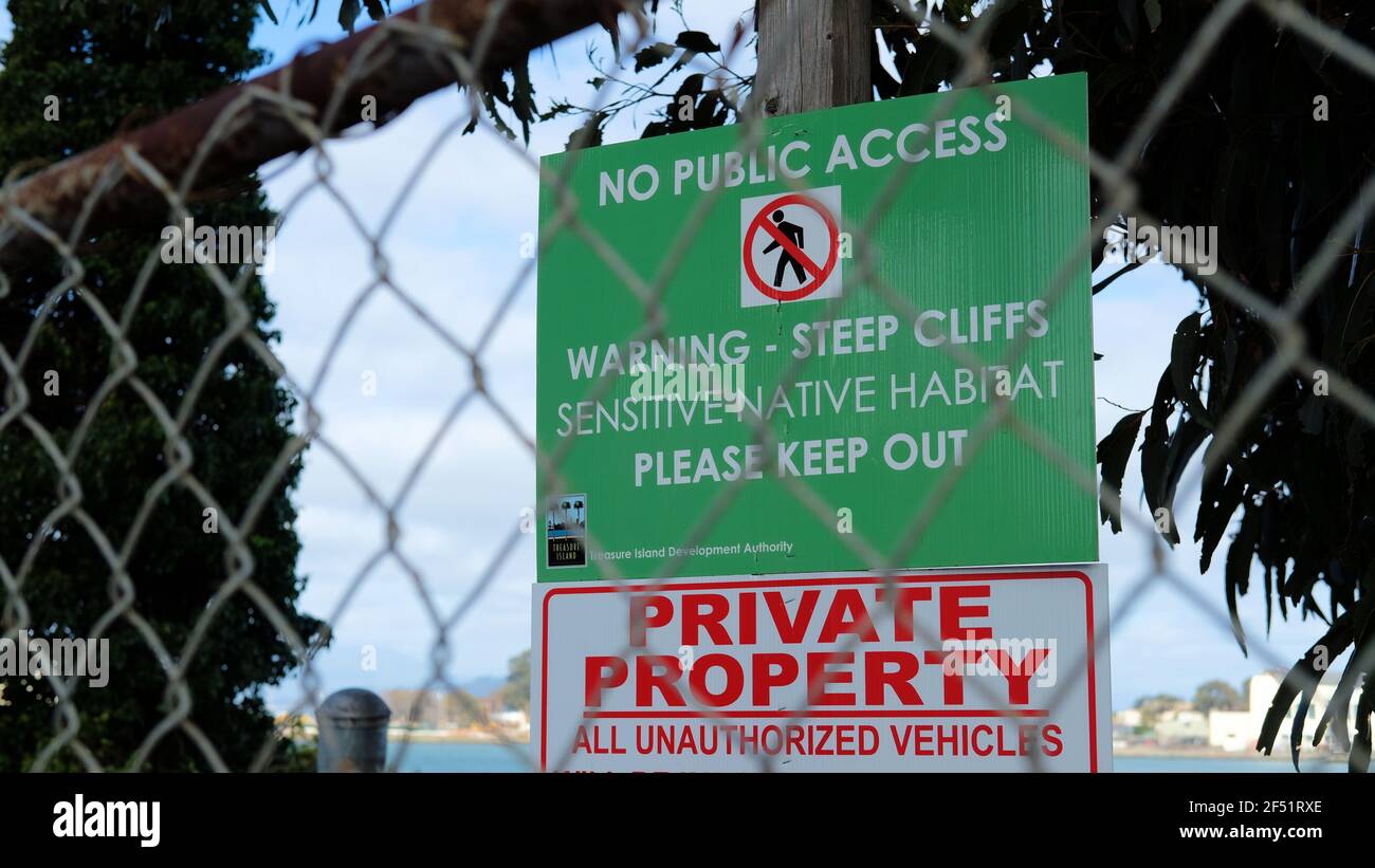 Grünes Warnschild durch einen Kettengliedzaun gesehen; steile Klippe, empfindlicher Lebensraum, Privateigentum; Yerba Buena Island, San Francisco, Caifornia. Stockfoto