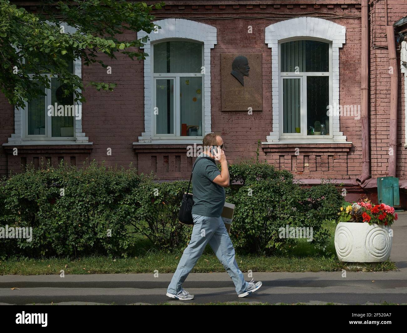 Ein Mann, der einen Anruf macht, während er an einer Gedenktafel an Wladimir Iljitsch Lenin im östlichen Verwaltungsbezirk von Moskau vorbeigeht. Stockfoto