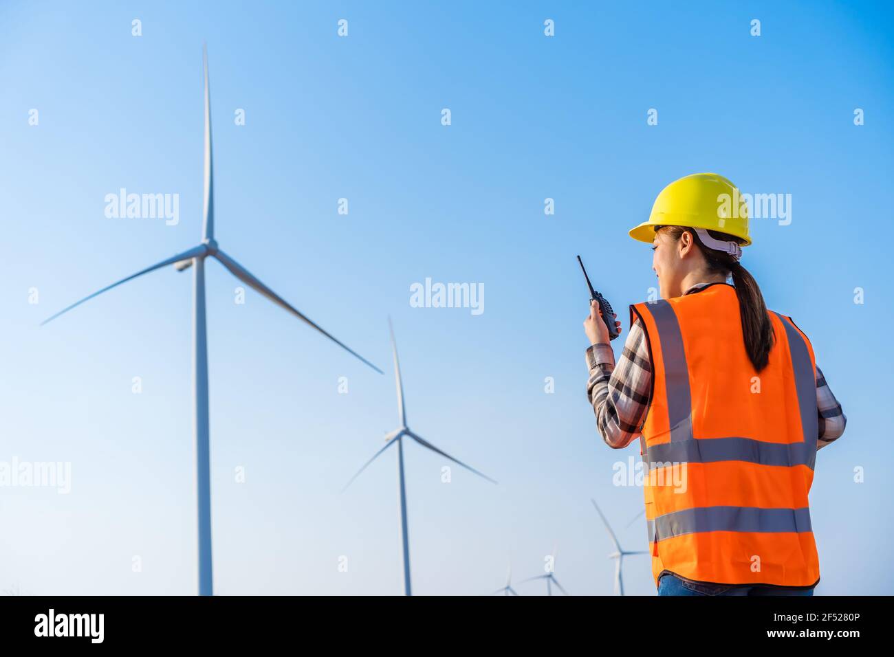 Junge Ingenieurin mit Walkie Talkie, um das System gegen zu überprüfen Windturbinenpark Stockfoto