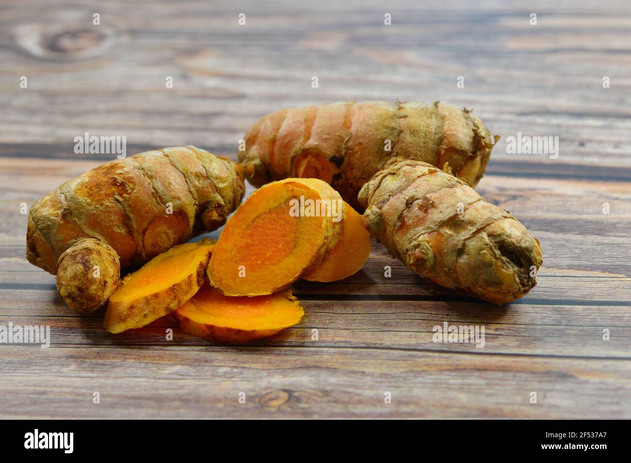 Nahaufnahme der Scheiben und der gesamten Kurkumenwurzel oder des Rhizoms. Die Wurzeln stammen aus dem indischen Subkontinent und werden in der Küche und ayurvedischen Medizin verwendet. Stockfoto