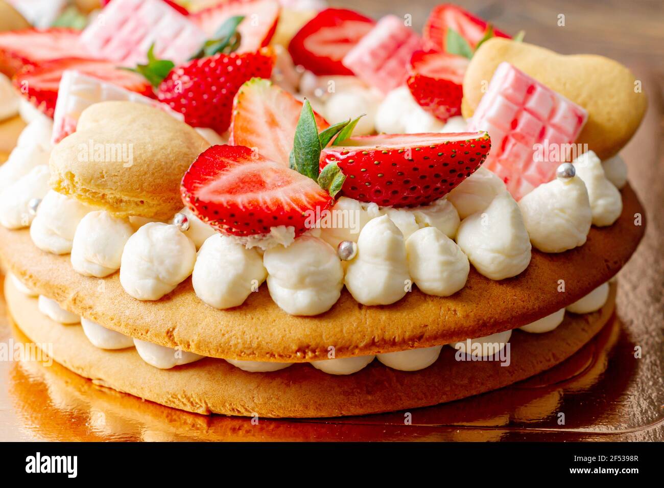 Biskuitkuchen mit Erdbeeren, rosa Milchschokolade, Silberstreuseln, Vanillecreme und herzkranken Keksen aus nächster Nähe. Sommer süßes Dessert für bi Stockfoto