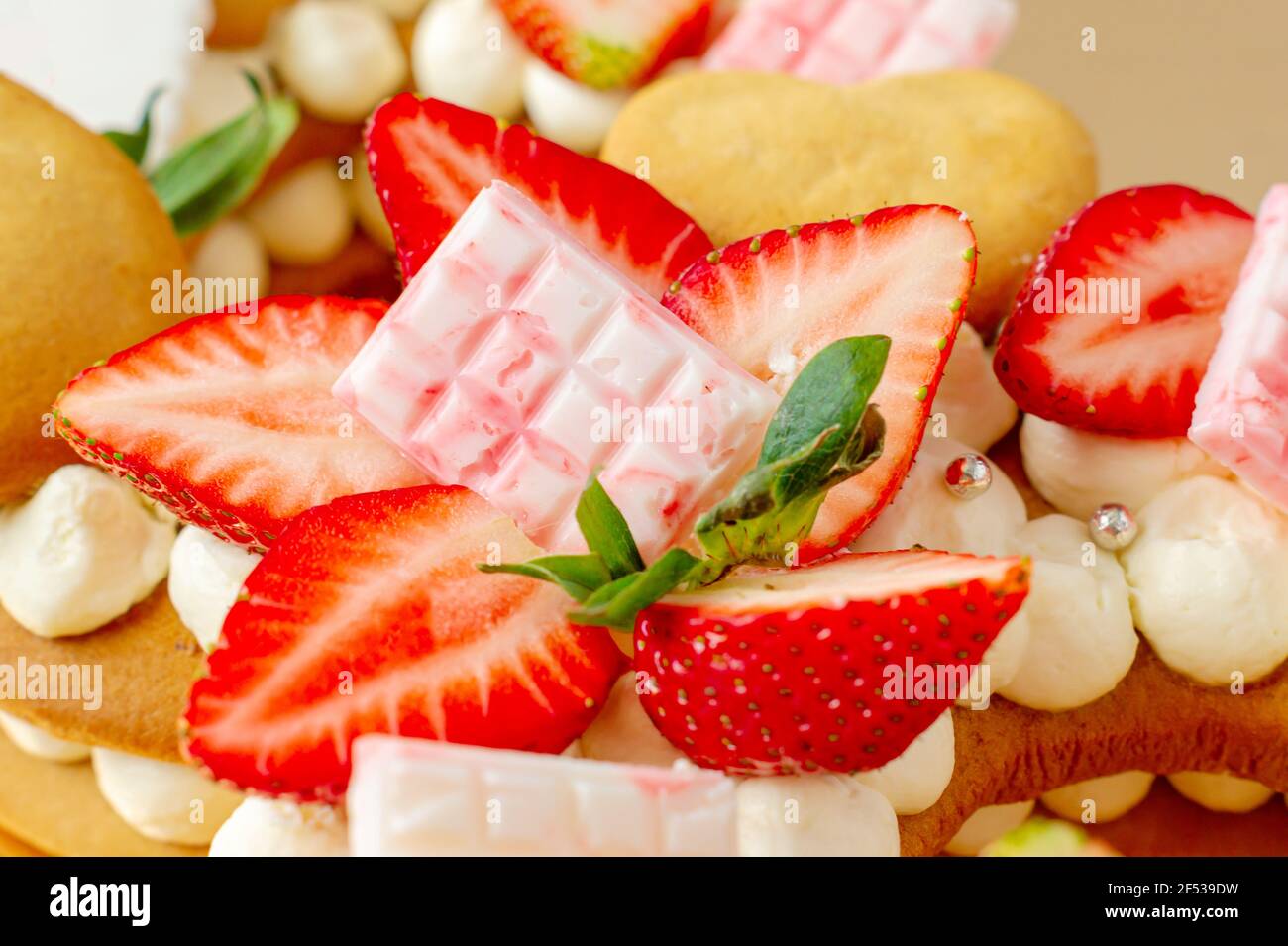 Biskuitkuchen mit Erdbeeren, rosa Milchschokolade, Silberstreuseln, Vanillecreme und herzkranken Keksen aus nächster Nähe. Sommer süßes Dessert für bi Stockfoto
