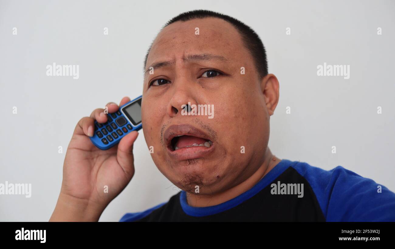 Ein asiatischer Mann mit kahlem Haar telefoniert mit einem alten Telefon mit seltsamem Ausdruck Stockfoto