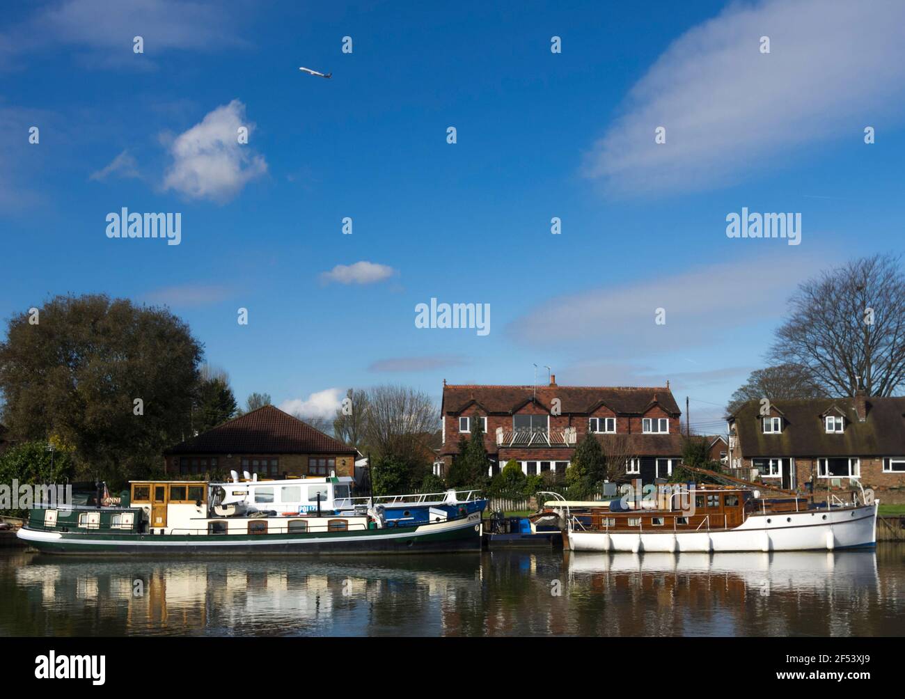 Die Boote liegen auf der Themse in Staines-upon-Thames, Surrey, Großbritannien, während ein Jet über der Themse vorbeifährt. Stockfoto
