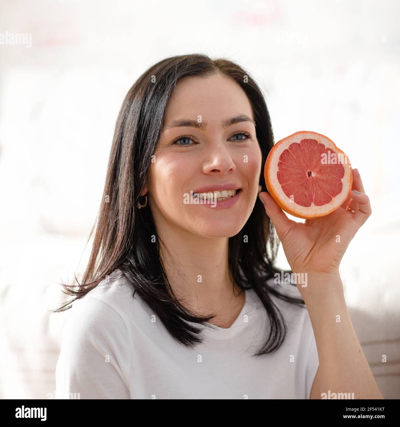 Lächelnde Frau in blauem Hemd, die Grapefruit in einer Küche hält Stockfoto