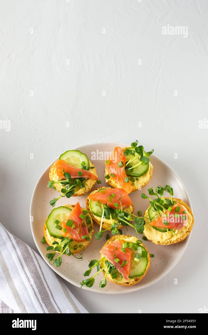 Leckere herzhafte Vorspeise, Lachsbraten auf einem weißen Teller, rundes gebratenes Brötchen mit rotem Fisch, Gurke, Sauce Hollandaise und Erbsensprossen Stockfoto