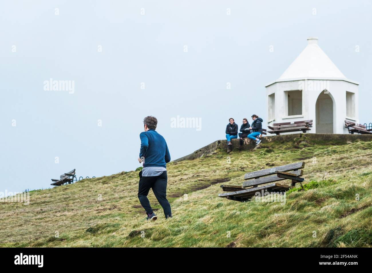 Ein Mann, der mit drei Frauen im Hintergrund auf dem Towan Head in Newquay in Cornwall läuft. Stockfoto
