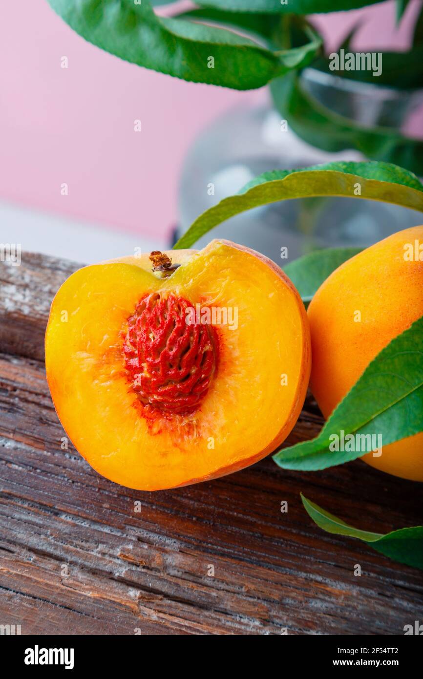 Pfirsich in Hälften mit Knochen. Pfirsiche mit Blättern auf Holzbrett. Reife saftige Pfirsiche. Frische Bio-Pfirsiche Obst für Lebensmittel auf rosa Hintergrund. Stockfoto