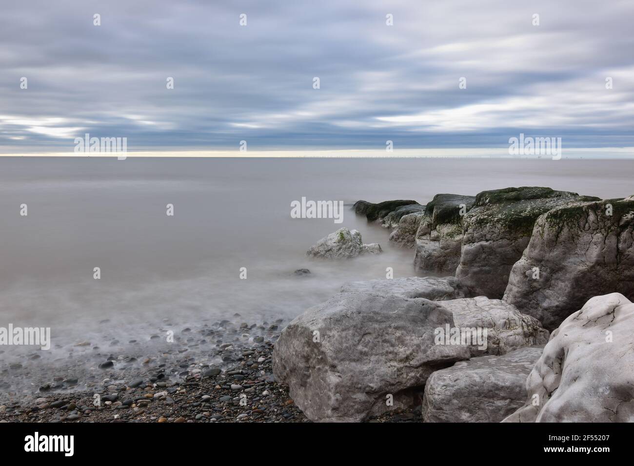 Felsen und Kieselsteine, die am Meer bei Cleveleys überspült werden Strand (nördlich von Blackpool) mit Bewegung verschwimmen zum Meer Stockfoto