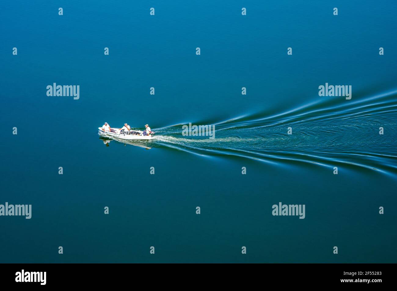 Weißes Fischerboot mit drei Personen an Bord schwimmt in einem See. Stockfoto