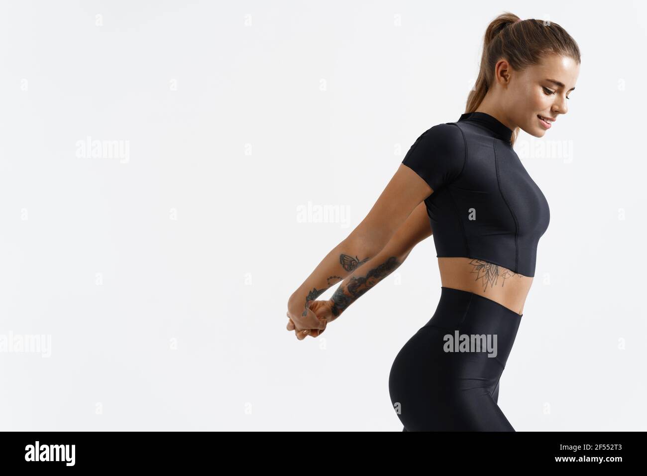 Fitness trainierte weibliche Stretching Arme hinter dem Rücken, dabei Aufwärmübungen. Läuferin mit feinem Körper trainieren vor dem Joggen in Sportswear, weiß Stockfoto