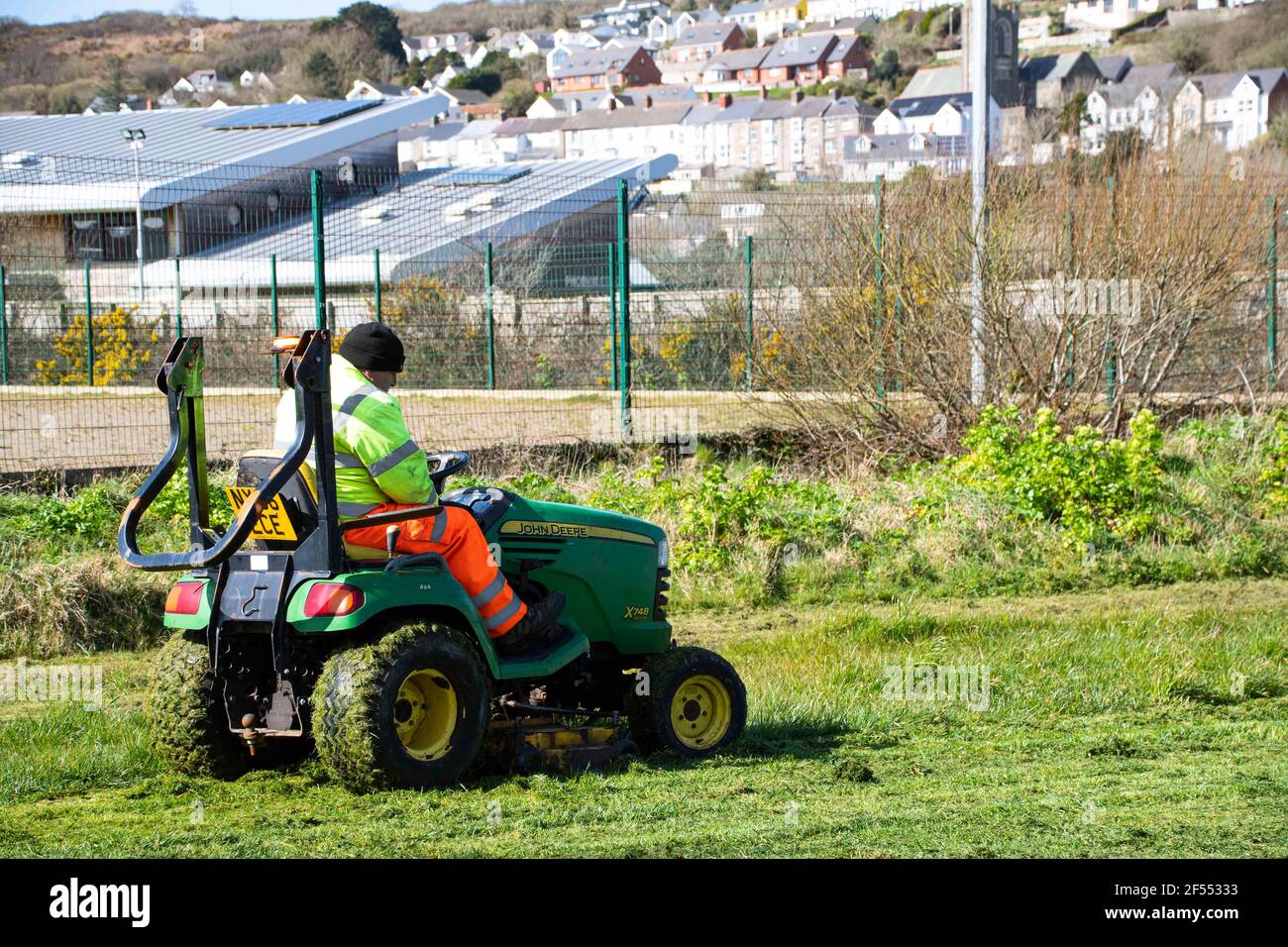 Fishguard, Pembrokeshire, großbritannien .24. März 2021. Arbeiter in ihren hohen VIS Jacken fahren auf Gras Schneider wie mehr Besucher ankommen, Pembrokeshire County Council hat daher eine schwierige, ein Gleichgewicht zu finden, da einige Schneiden ist wichtig für die Sicherheit Zwecke, aber es ist sehr daran interessiert, al wilde Tiere gedeihen, wo immer möglich. . Kredit: Debra Angel/Alamy Live Nachrichten Stockfoto