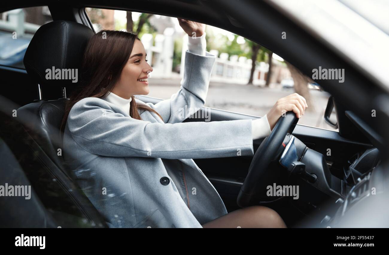 Unternehmen. Glückliche busienswoman Auto fahren und winken Hand an Freund. Elegante weibliche Fahrerin, die sich auf die Konferenz begibt und hallo sagt Stockfoto