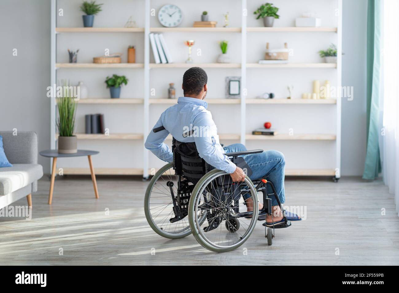 Depression bei Erwachsenen mit Behinderung. Unglücklich junger schwarzer Mann im Rollstuhl Gefühl einsam zu Hause, voller Länge Stockfoto