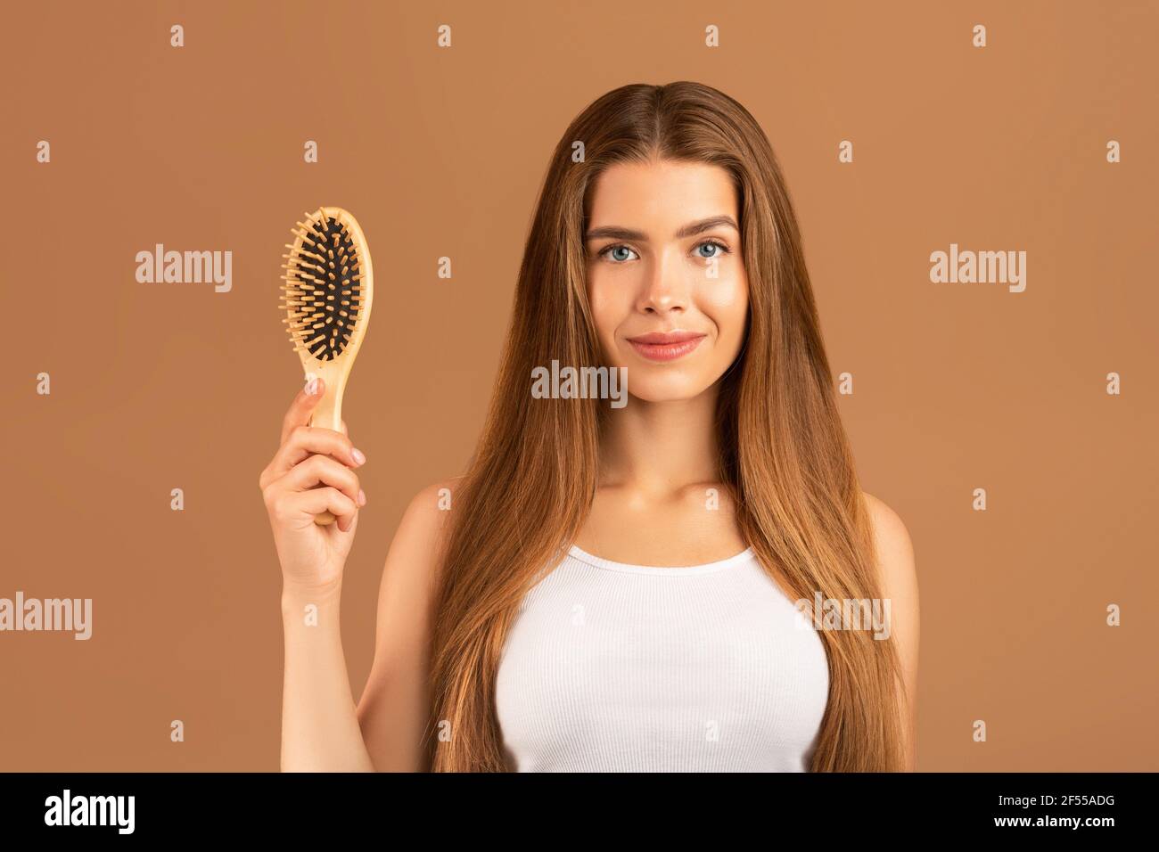 Haarpflegekonzept. Schöne junge Dame mit schönen Frisur hält Holzhaarbürste auf braunen Studio-Hintergrund Stockfoto