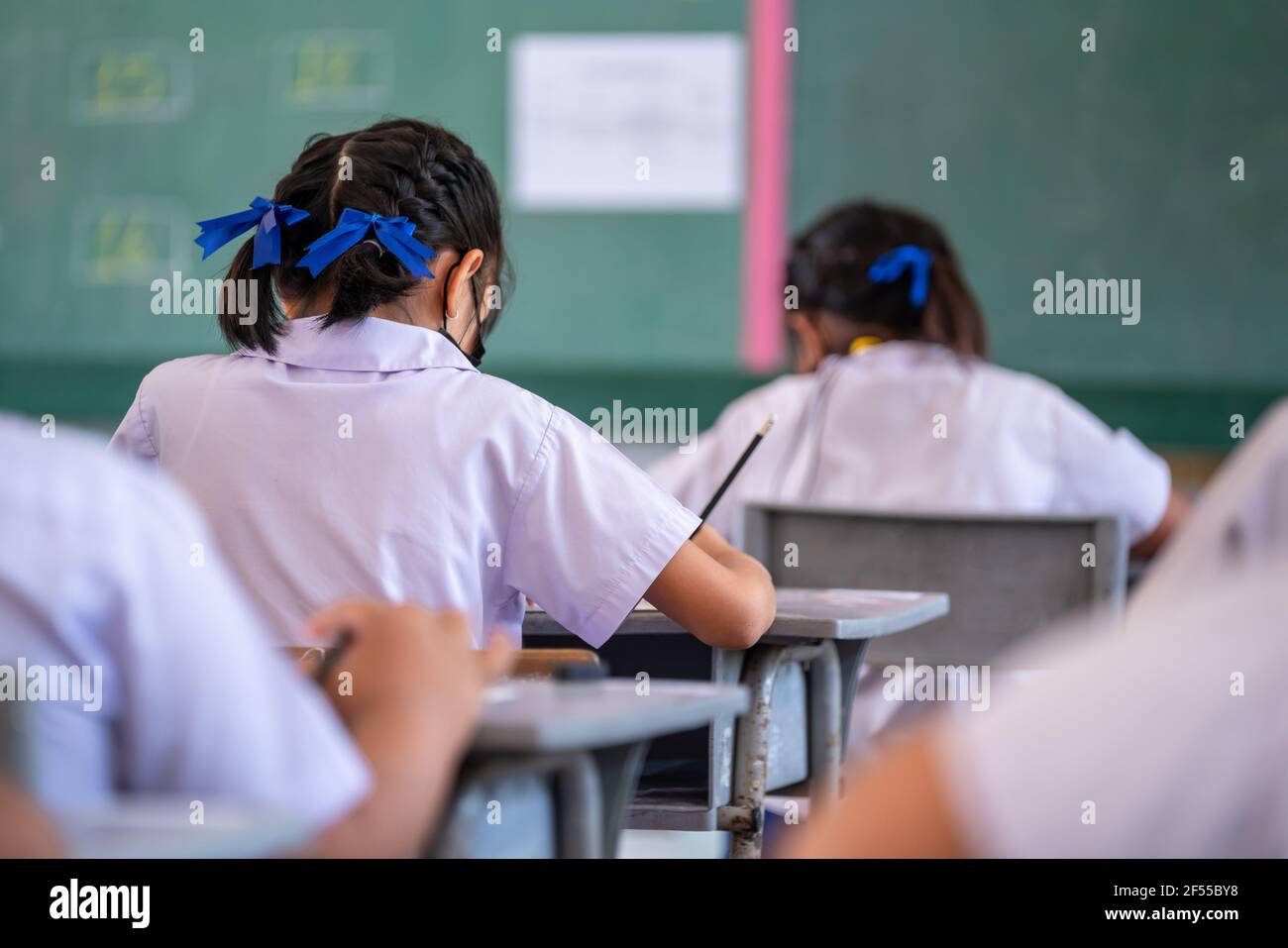 Nahaufnahme des Schreibstests in der Prüfung mit hinter Kind asiatische Schüler Gruppe konzentrieren sich in der Grundschule, Abschlussprüfung Schreibtisch im Klassenzimmer mit Thai s Stockfoto