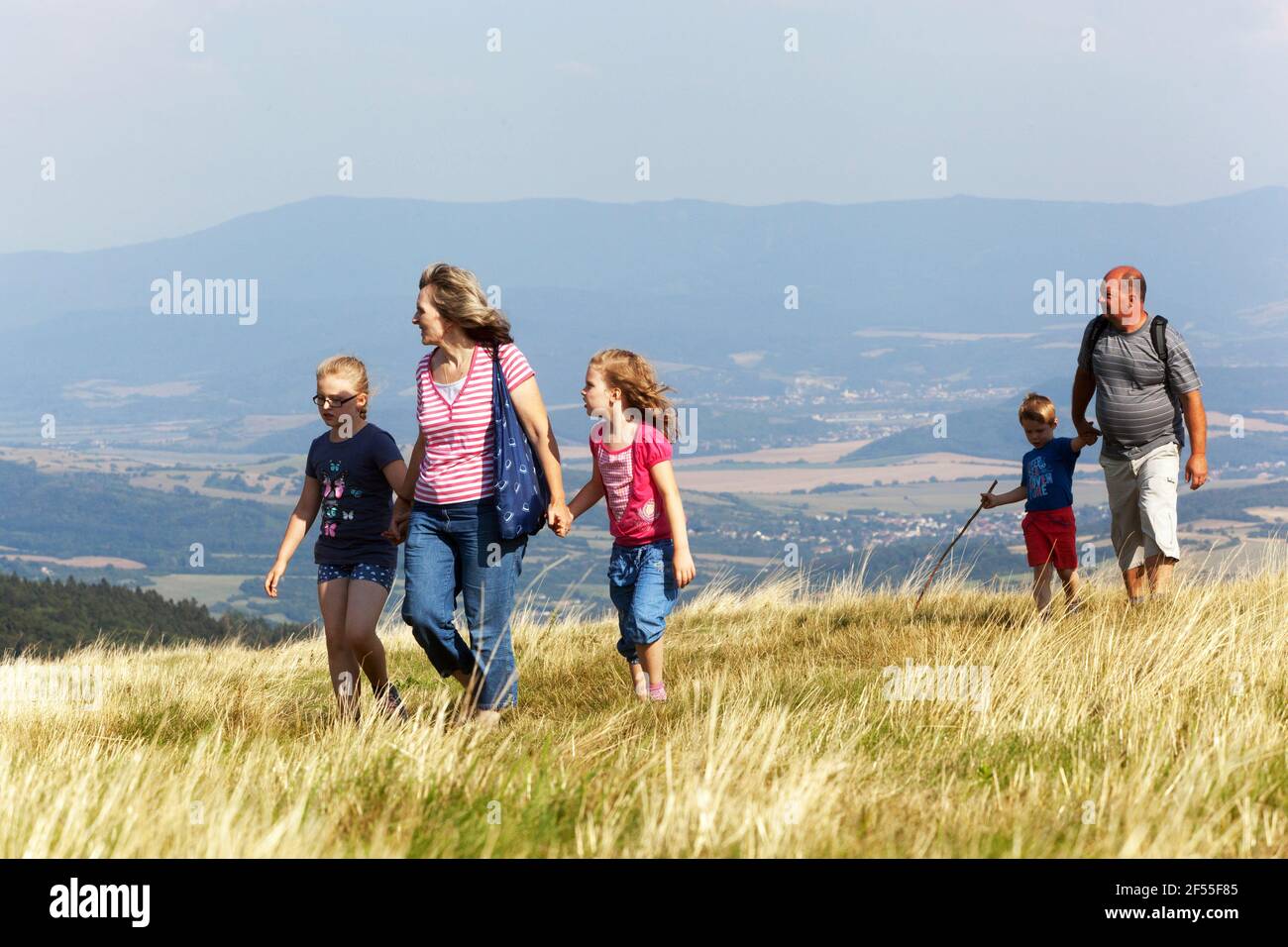 Familie mit Kindern auf einer Reise, aktive Großeltern, Mädchen, Kinder halten die Hände und gehen auf der Wiese Stockfoto