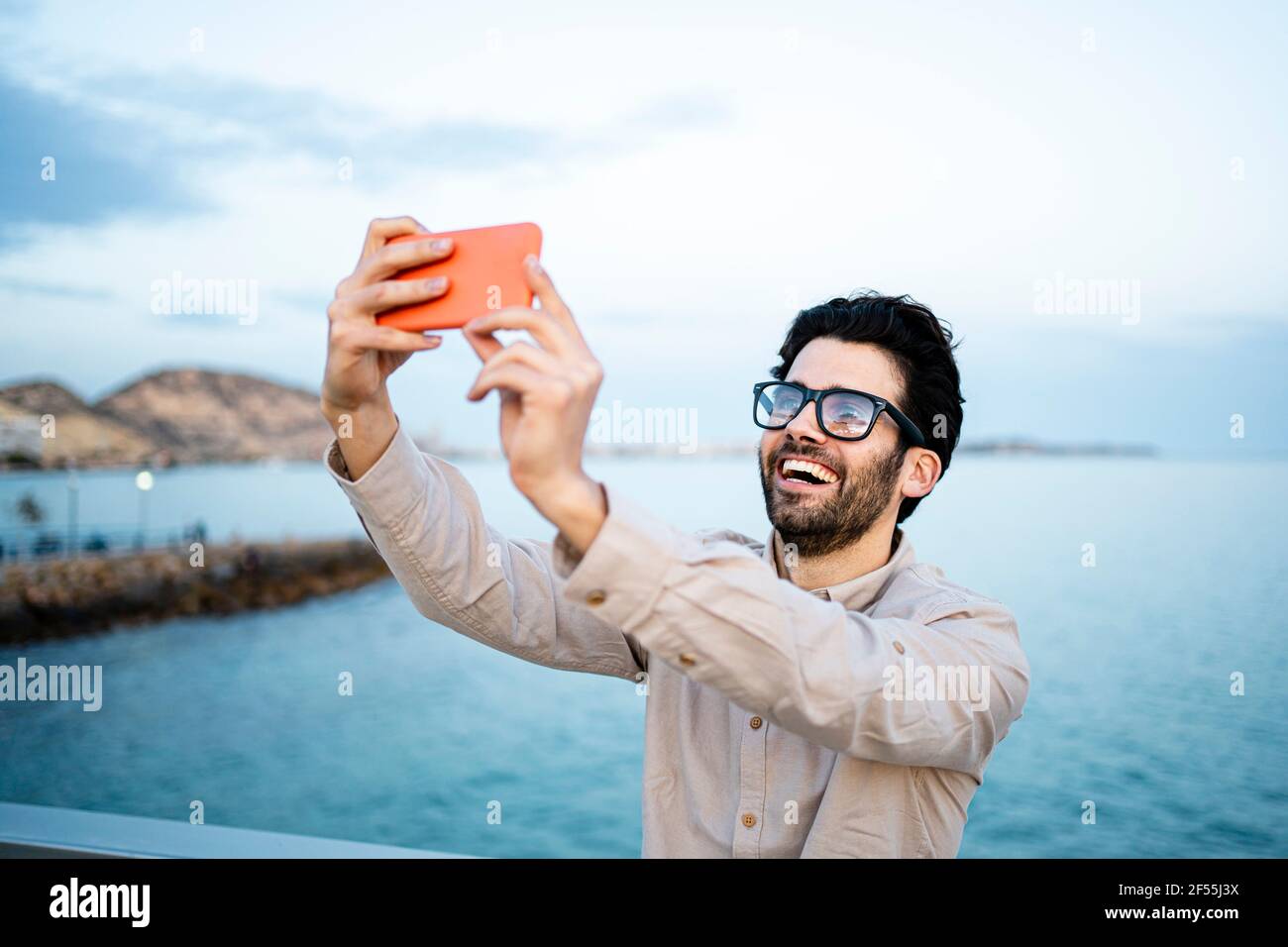 Fröhlicher Geschäftsmann, der am Meer Selfie per Handy nimmt Stockfoto