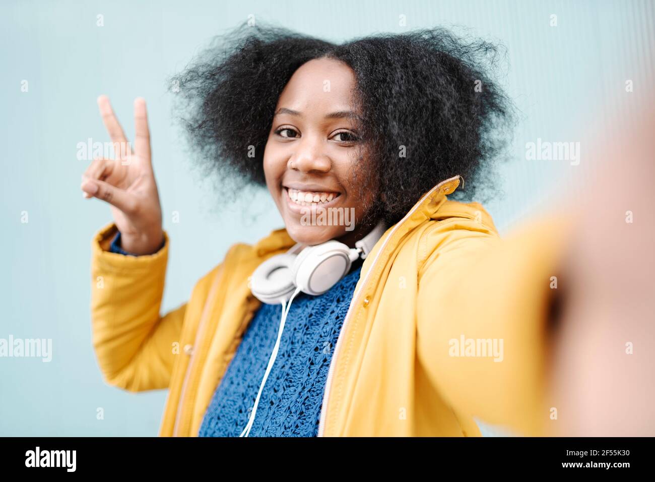 Junge Frau tut Friedenszeichen gegen Wand Stockfoto