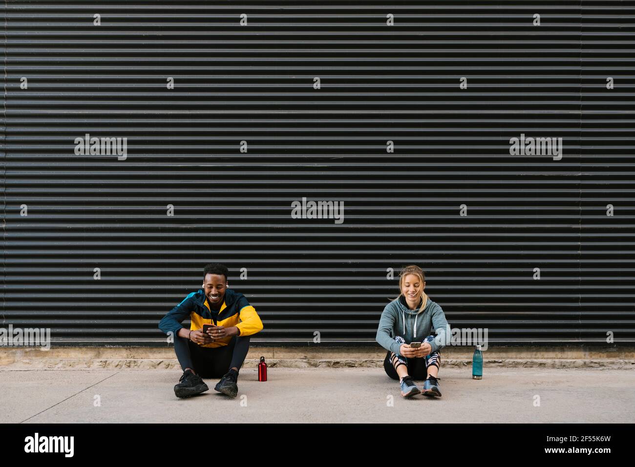 Männliche und weibliche Sportsperson, die Mobiltelefon benutzt, während sie dagegen sitzt Wand Stockfoto