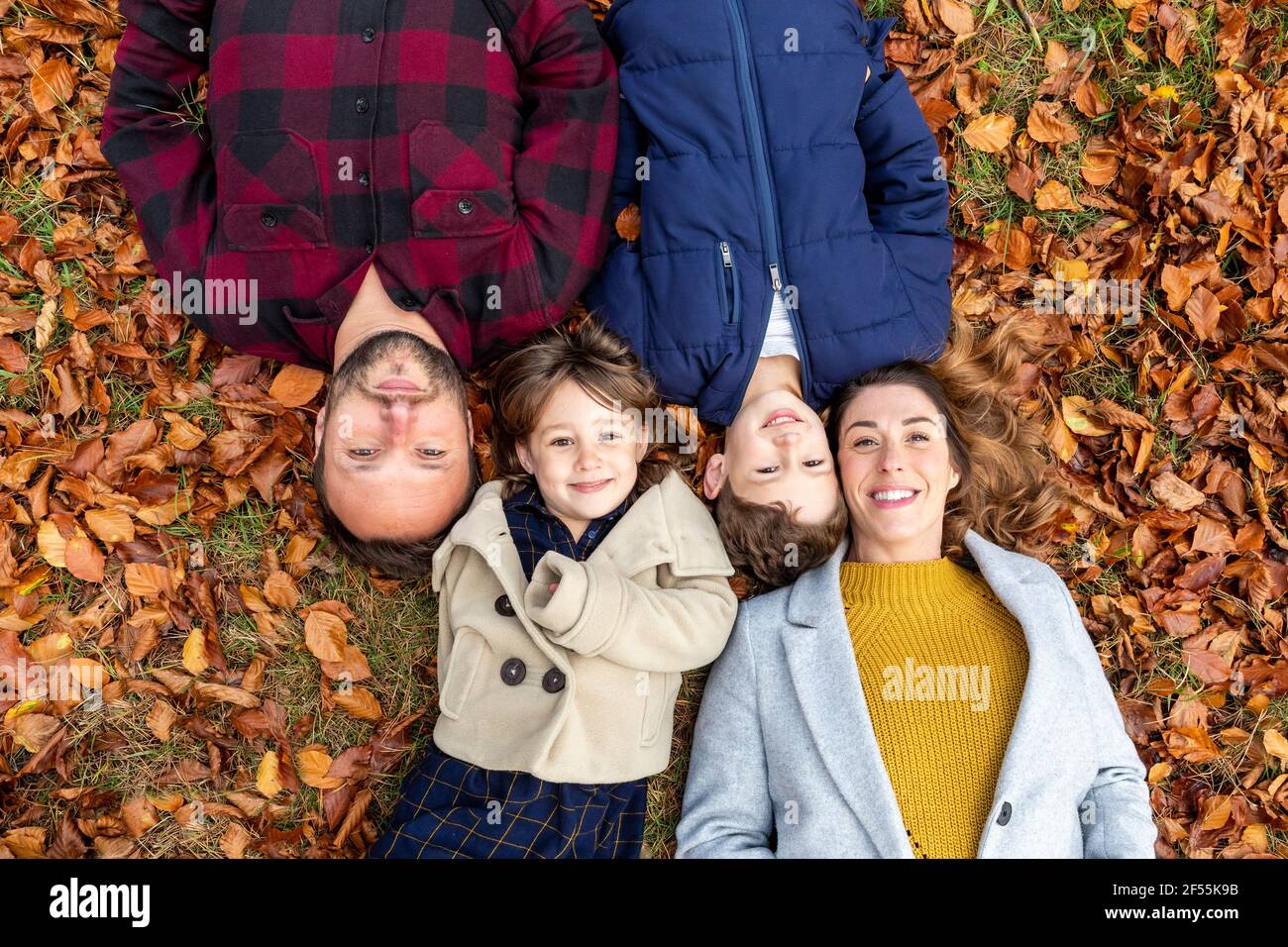 Lächelnde Familie, die im Herbst auf einem gefallenen Blatt im Wald liegt Stockfoto