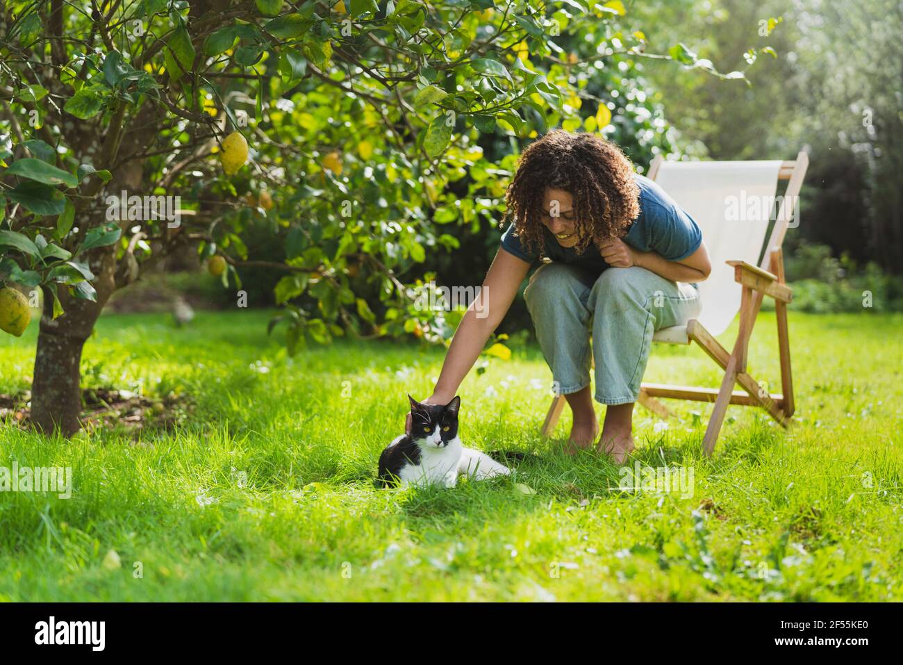 Die lockige Frau streichelte die Katze, während sie auf dem Stuhl saß Garten Stockfoto