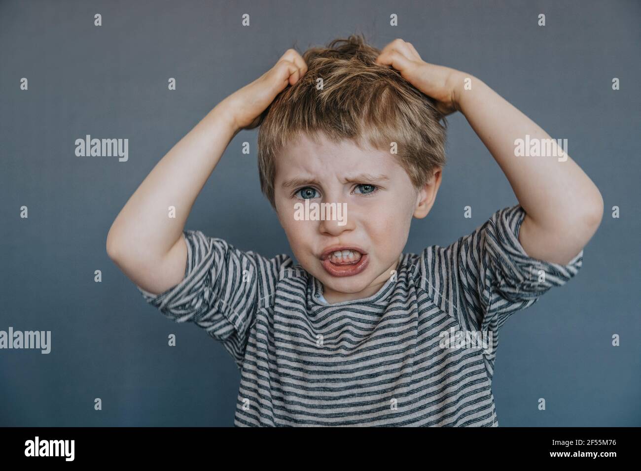 Frustrierter Junge kratzt den Kopf vor grauem Hintergrund Stockfoto