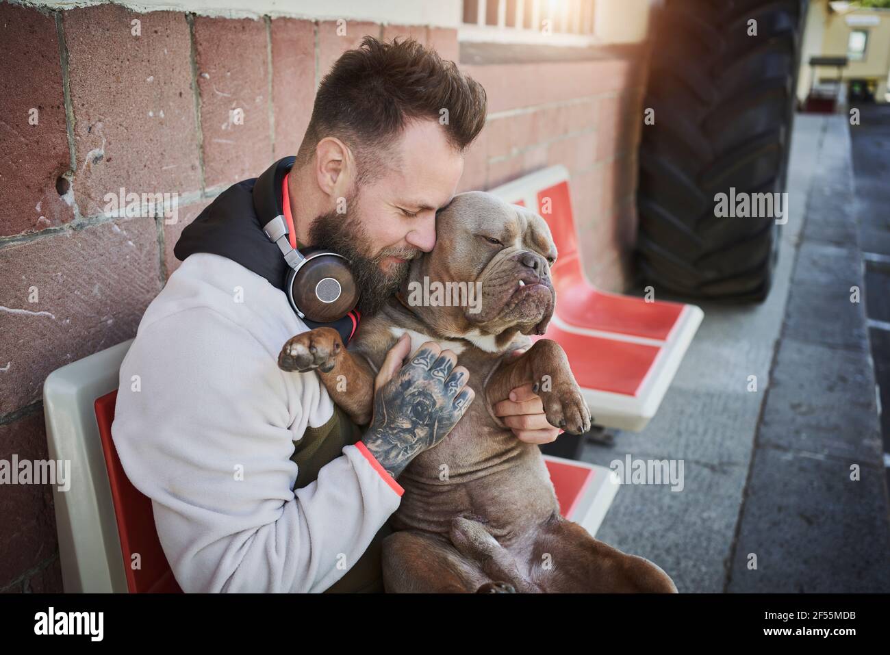 Männlicher Fitness-Trainer umarmt Bulldogge vor dem Fitnessstudio Stockfoto