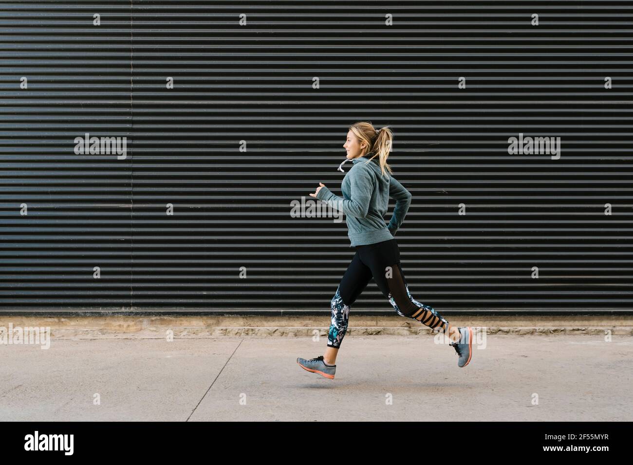 Weibliche Sportlerin, die während des Sporttrainings auf dem Bürgersteig an der Wand läuft Stockfoto