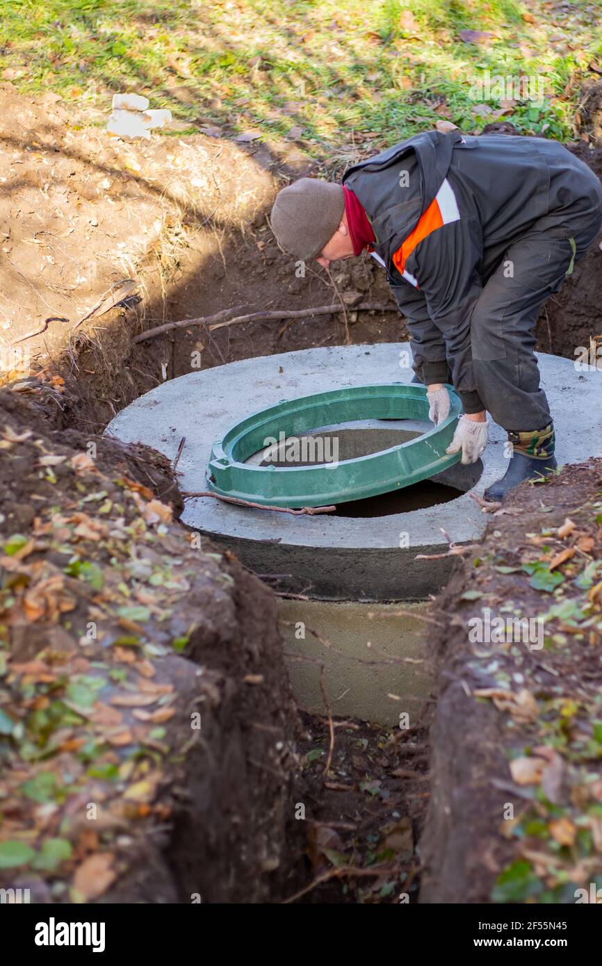 Ein Arbeiter installiert einen Kanalschacht an einem Klärbecken aus Betonringen. Bau von Abwasserentsorgungsanlagen für Privathäuser. Stockfoto