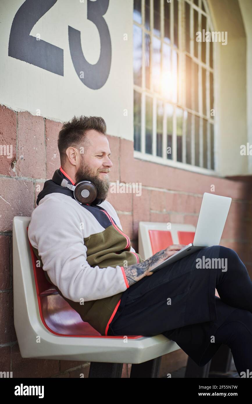 Männlicher Fitnesstrainer mit Laptop, während er vor dem Fitnessstudio sitzt Stockfoto