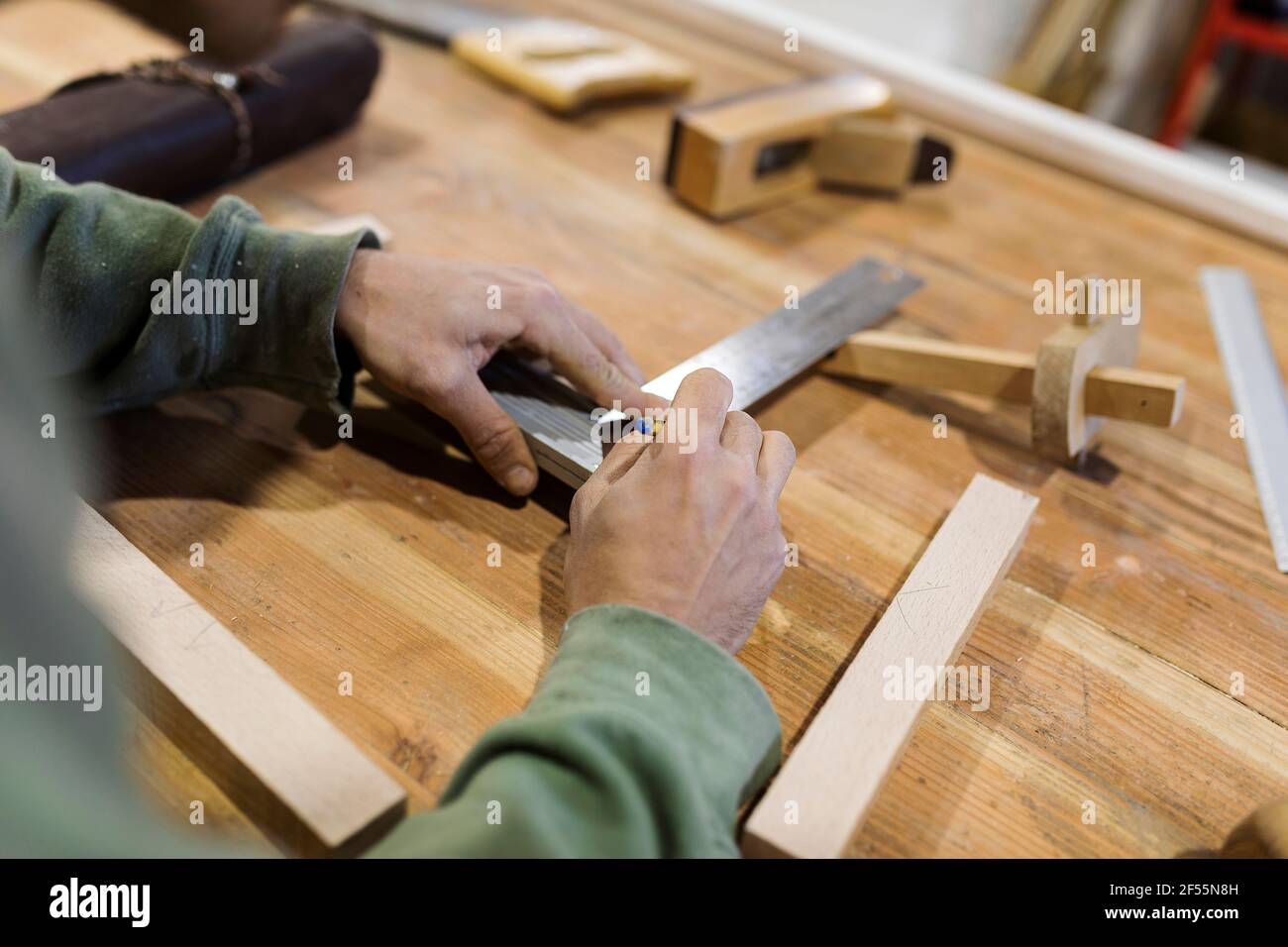 Männlicher Zimmermann, der in der Werkstatt Holzmaterial auf dem Tisch misst Stockfoto