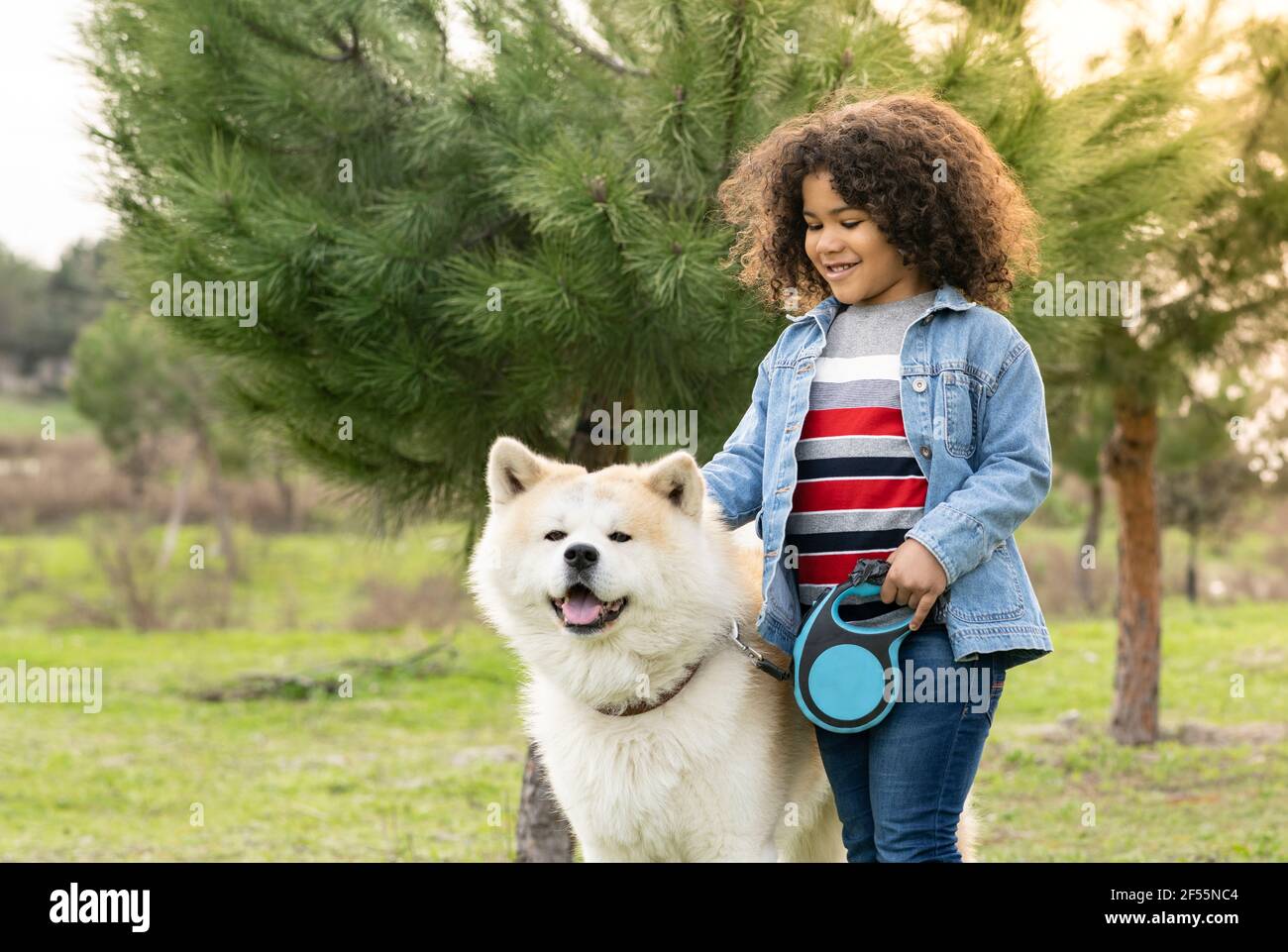 Lächelnder, lockiger Junge, der mit Hund in der Natur Spaß hat Stockfoto