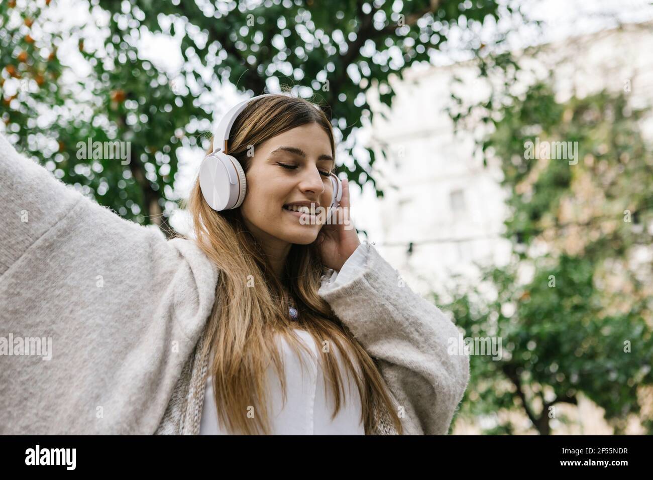 Fröhliche Frau, die im Freien Musik über Kopfhörer hört Stockfoto