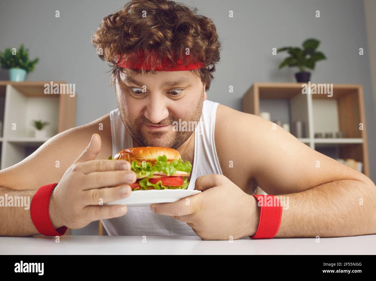 Lustige mollige Kerl in Sportbekleidung wird durch ungesunde versucht Aber leckere Burger Stockfoto