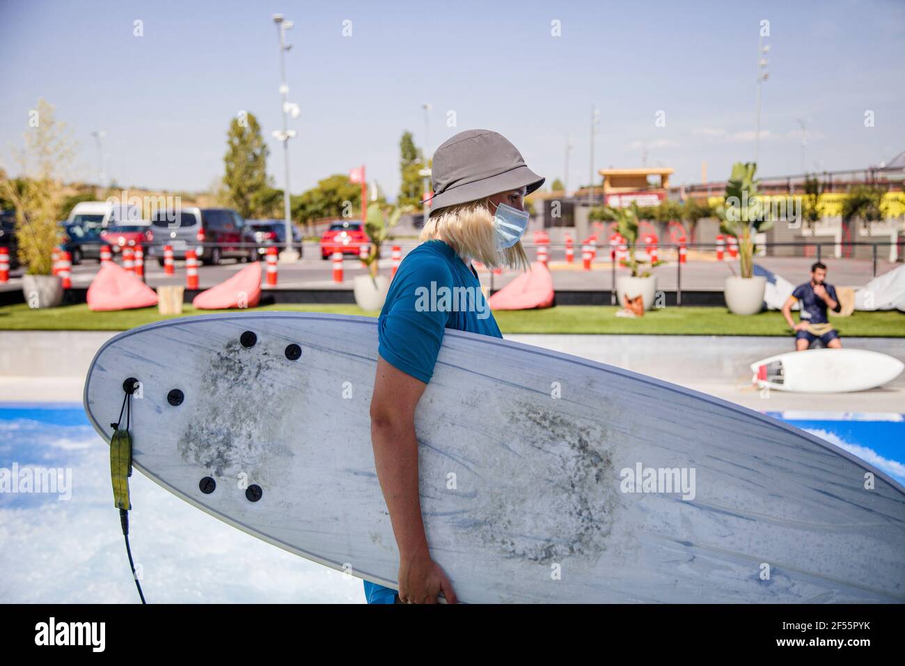 Weibliche Arbeiterin in Eimer Hut trägt Surfbrett während der Arbeit während COVID-19 Stockfoto